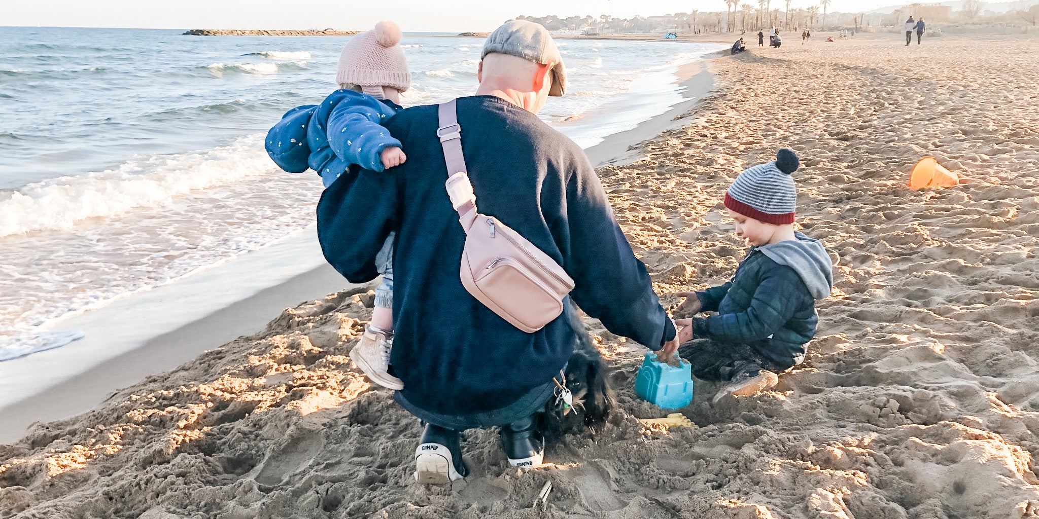 Dad wearing Kibou dad diaper bag in blush with kids on beach